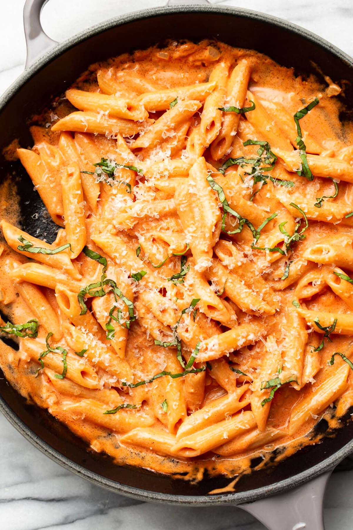 Creamy penne pasta in tomato sauce, topped with grated cheese and fresh basil, served in a black skillet—perfect for lovers of Italian pasta recipes.