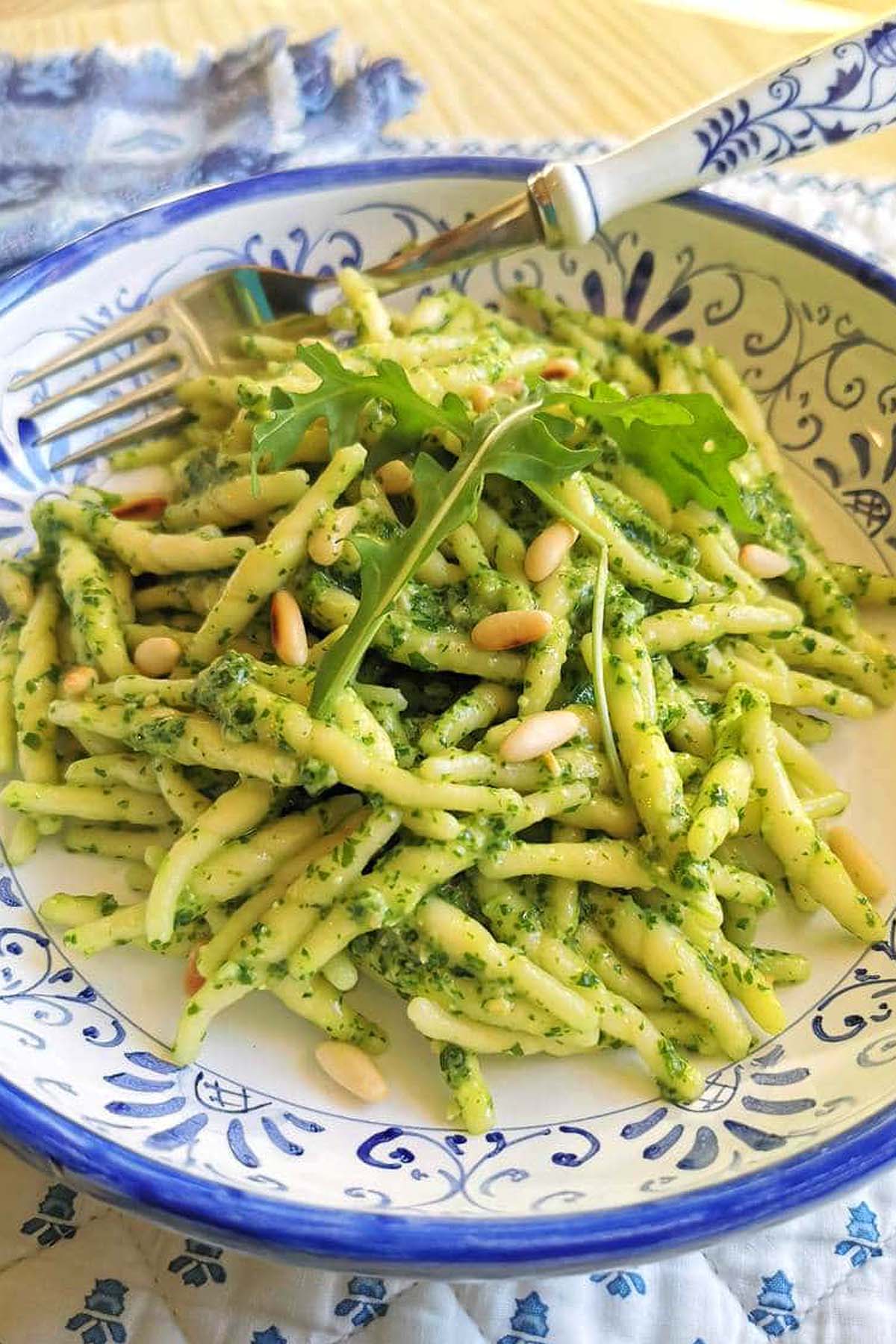 Trofie pasta with pesto sauce, arugula, and pine nuts served in a decorative plate with a fork—a delicious example of classic Italian pasta recipes.