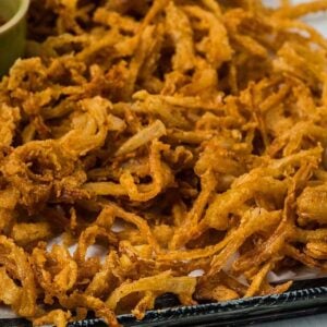 Golden crispy onion strings piled high on a tray, served with flavorful dipping sauces in small bowls on the side.