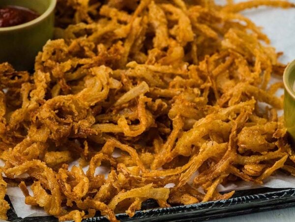 Golden crispy onion strings piled high on a tray, served with flavorful dipping sauces in small bowls on the side.