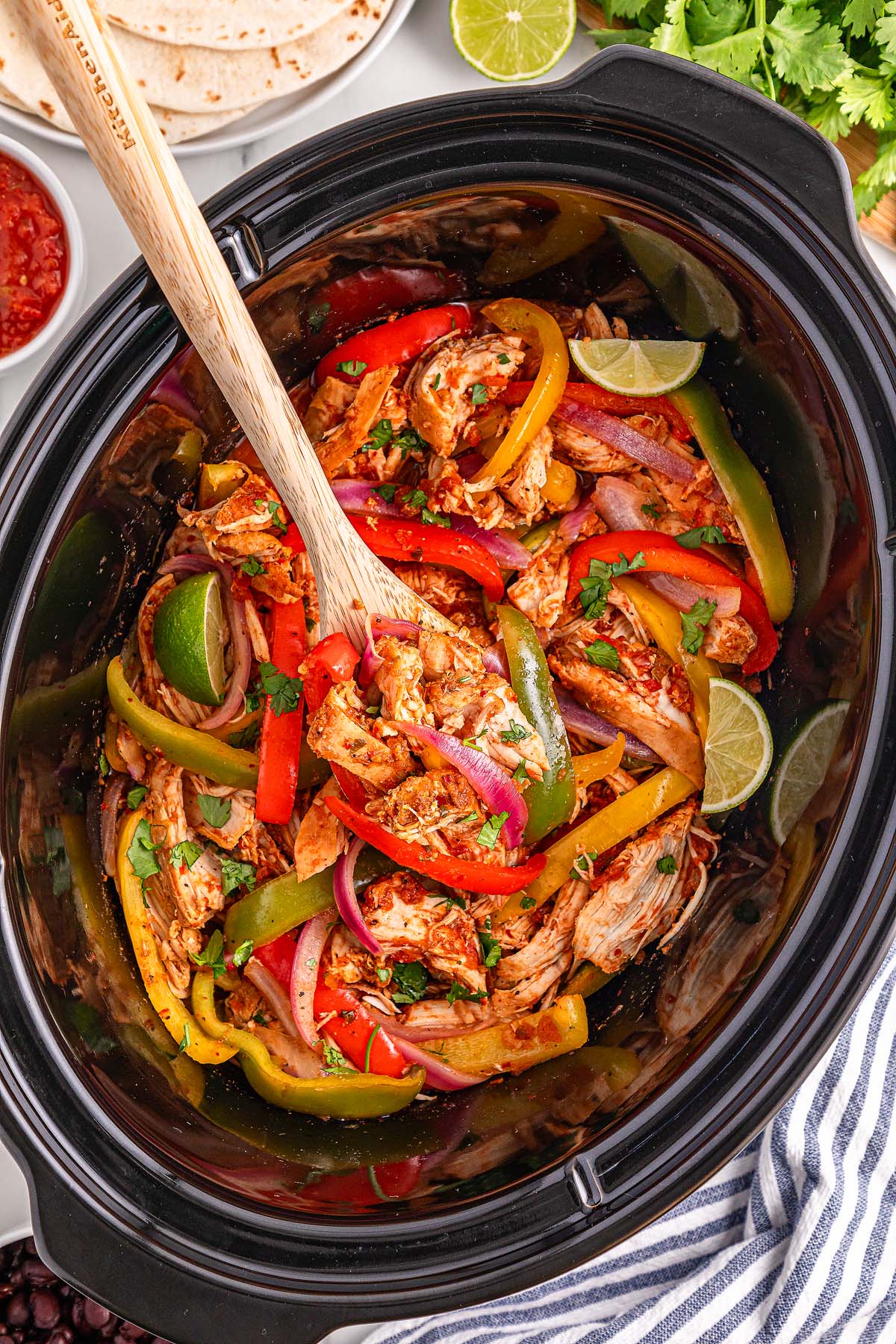 Slow cooker filled with shredded chicken, bell peppers, and onions, garnished with cilantro and lime wedges for flavorful Slow Cooker Chicken Fajitas.