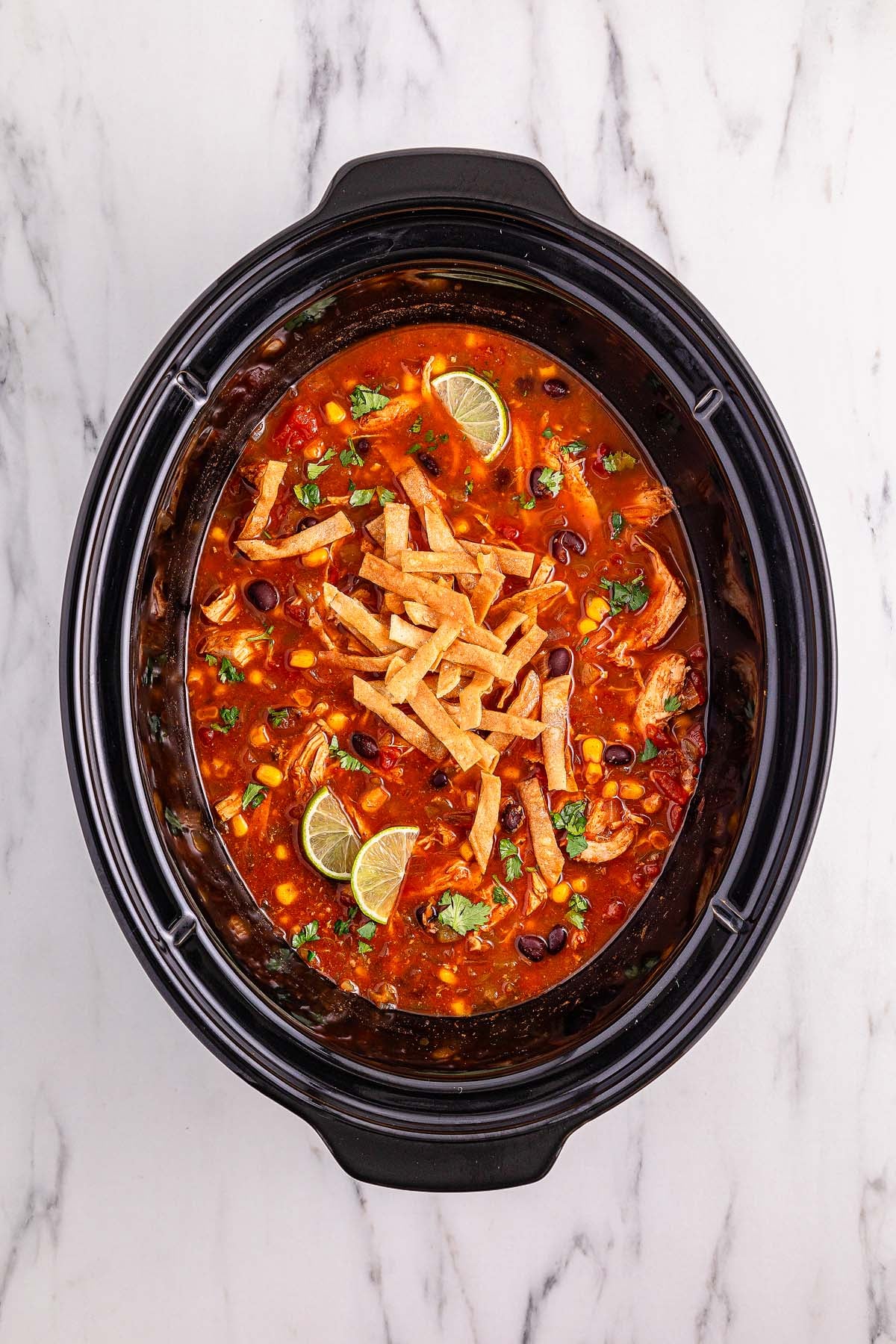 Slow Cooker Chicken Tortilla Soup simmers gently in a slow cooker, filled with tender chicken and hearty vegetables, then topped with crispy tortilla strips, fresh lime wedges, and cilantro for a flavorful finish.