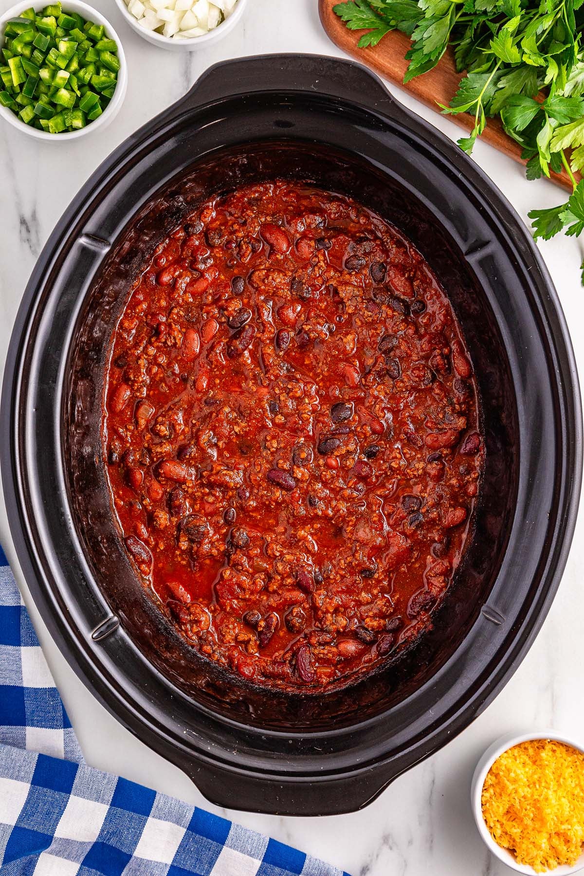 Slow cooker chili with beans and ground meat simmering to perfection, surrounded by chopped veggies and shredded cheese.
