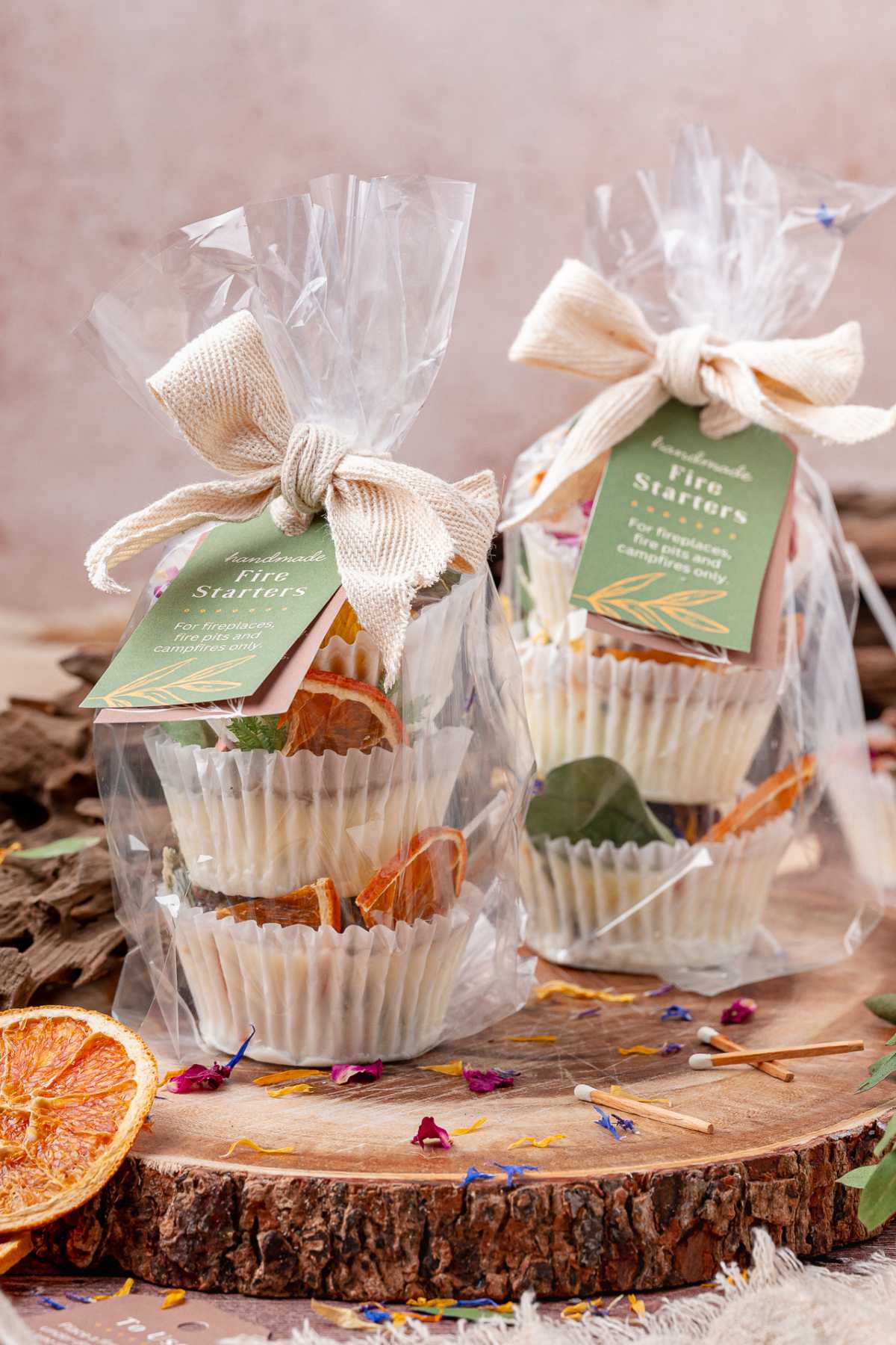 Two gift-wrapped packages of homemade fire starters with dried orange slices, displayed on a wooden surface.