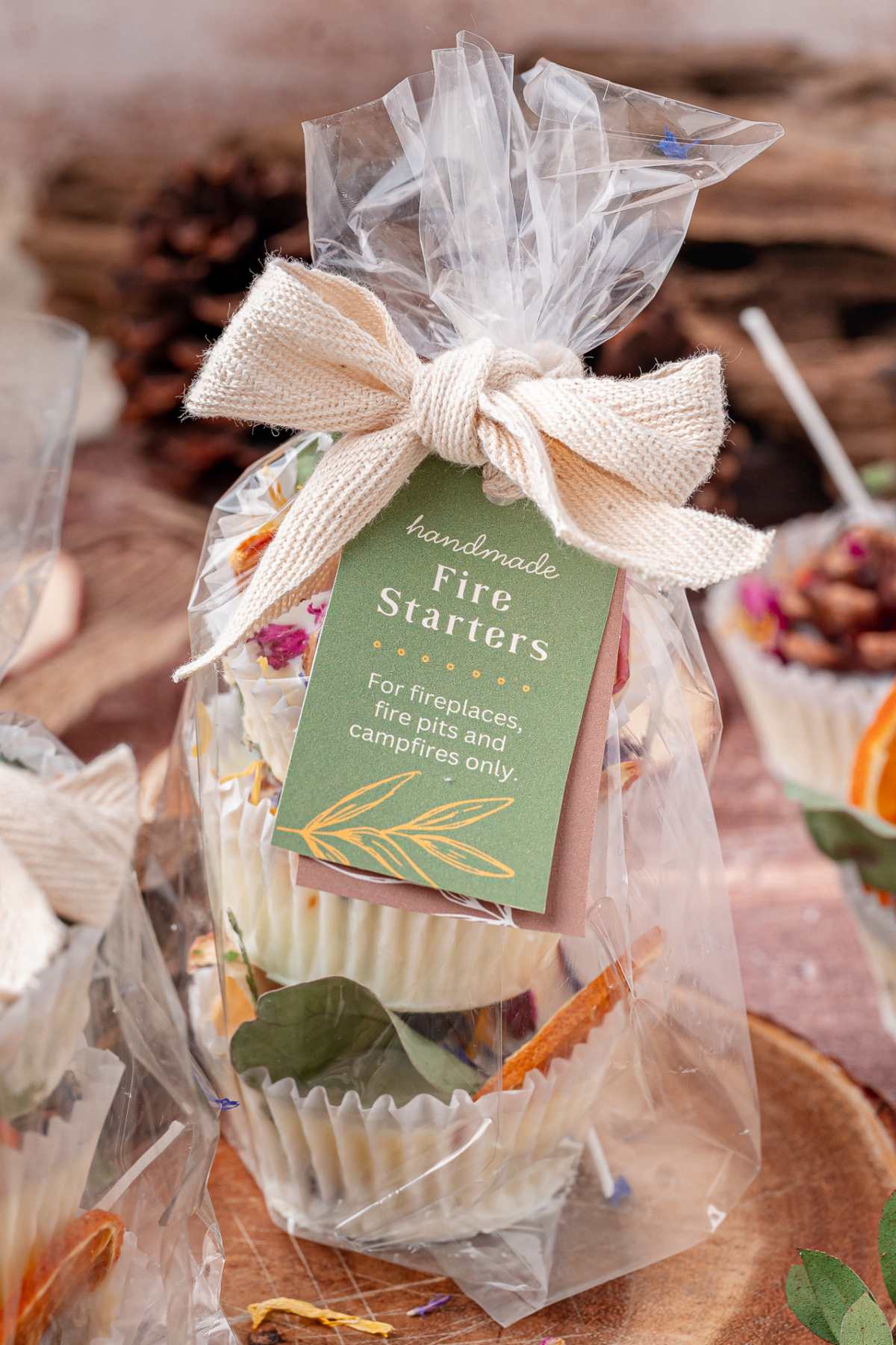 Gift-wrapped handmade fire starters with a green tag and a burlap bow, placed on a wooden surface.