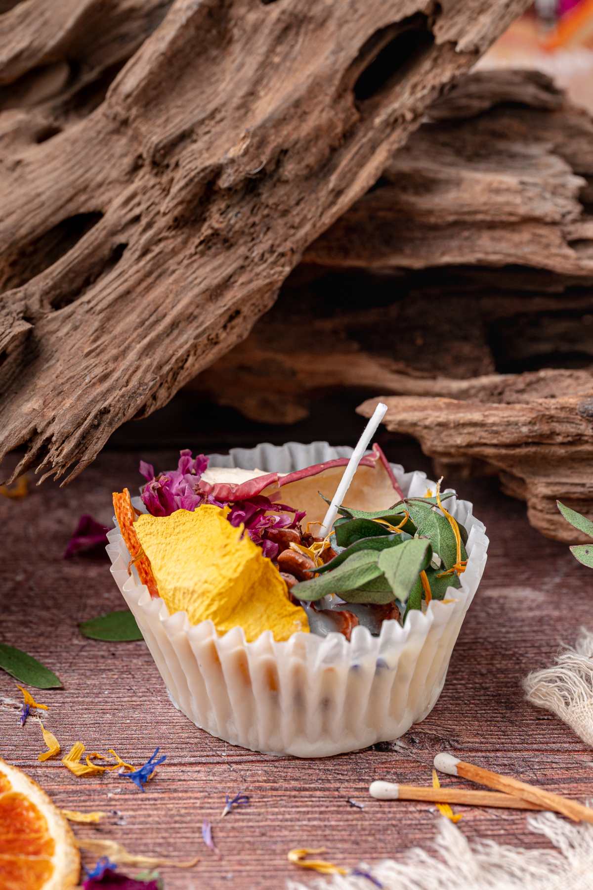 A fire starter in a white liner filled with dried flowers, and leaves sits in front of rustic wood.