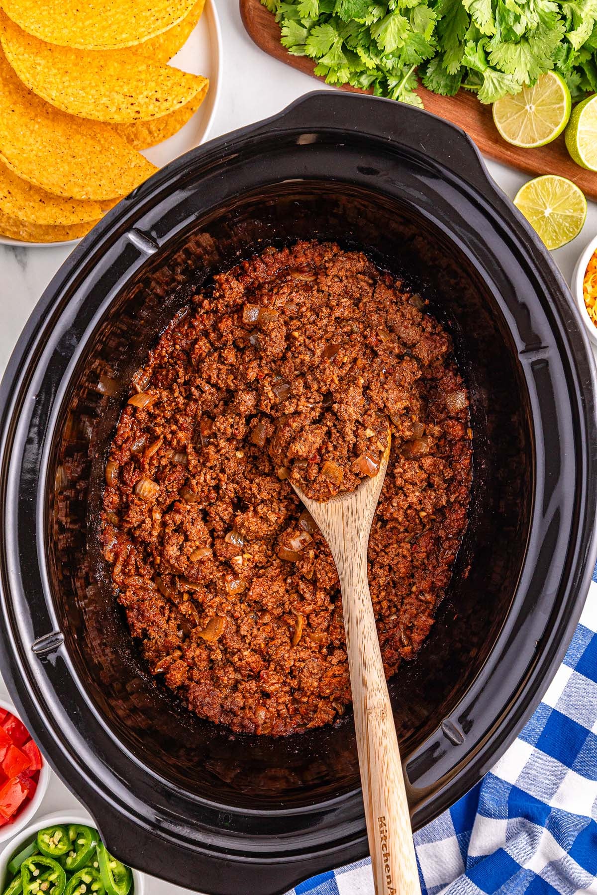 Slow Cooker Taco Meat simmers to perfection as ground beef taco filling in a slow cooker with a wooden spoon, surrounded by crispy taco shells and fresh toppings.
