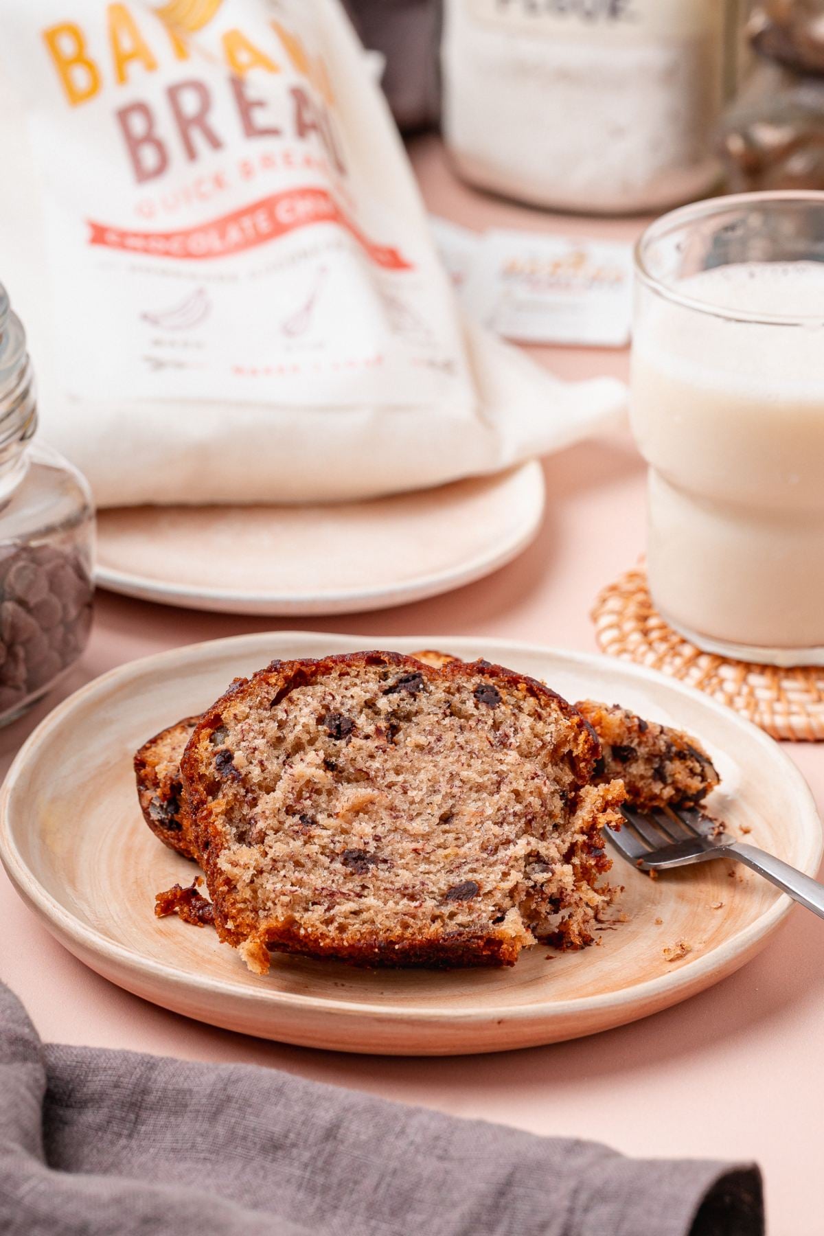 Two slices of chocolate chip banana bread, made with our homemade banana bread mix, rest on a plate alongside a glass of milk and a fork.