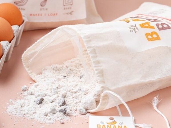 A bag of homemade banana bread mix spilled on a counter, with eggs, walnuts, and recipe cards.