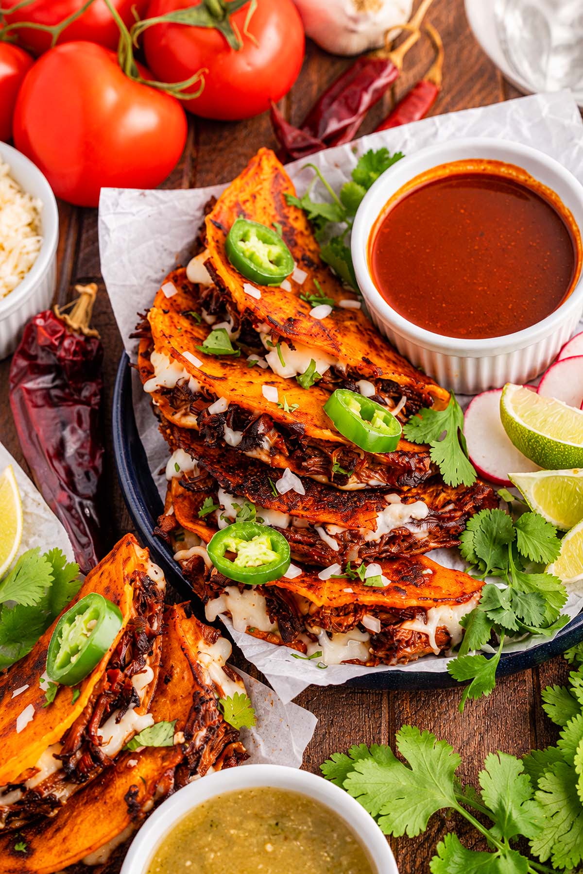 A plate of slow cooker birria tacos with lime wedges, fresh cilantro, salsa, and a bowl of dipping consommé.