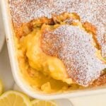 A lemon dump cake in a baking dish, dusted with powdered sugar, with a serving scooped out.