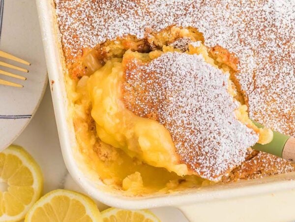 A lemon dump cake in a baking dish, dusted with powdered sugar, with a serving scooped out.