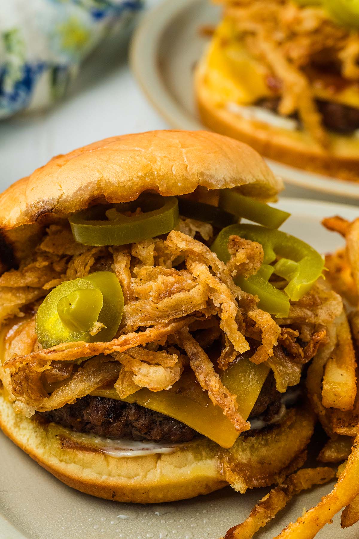 Saddle up for our cowboy burger: a juicy cheeseburger topped with crispy fried onions and spicy jalapenos, served with fries on a plate.