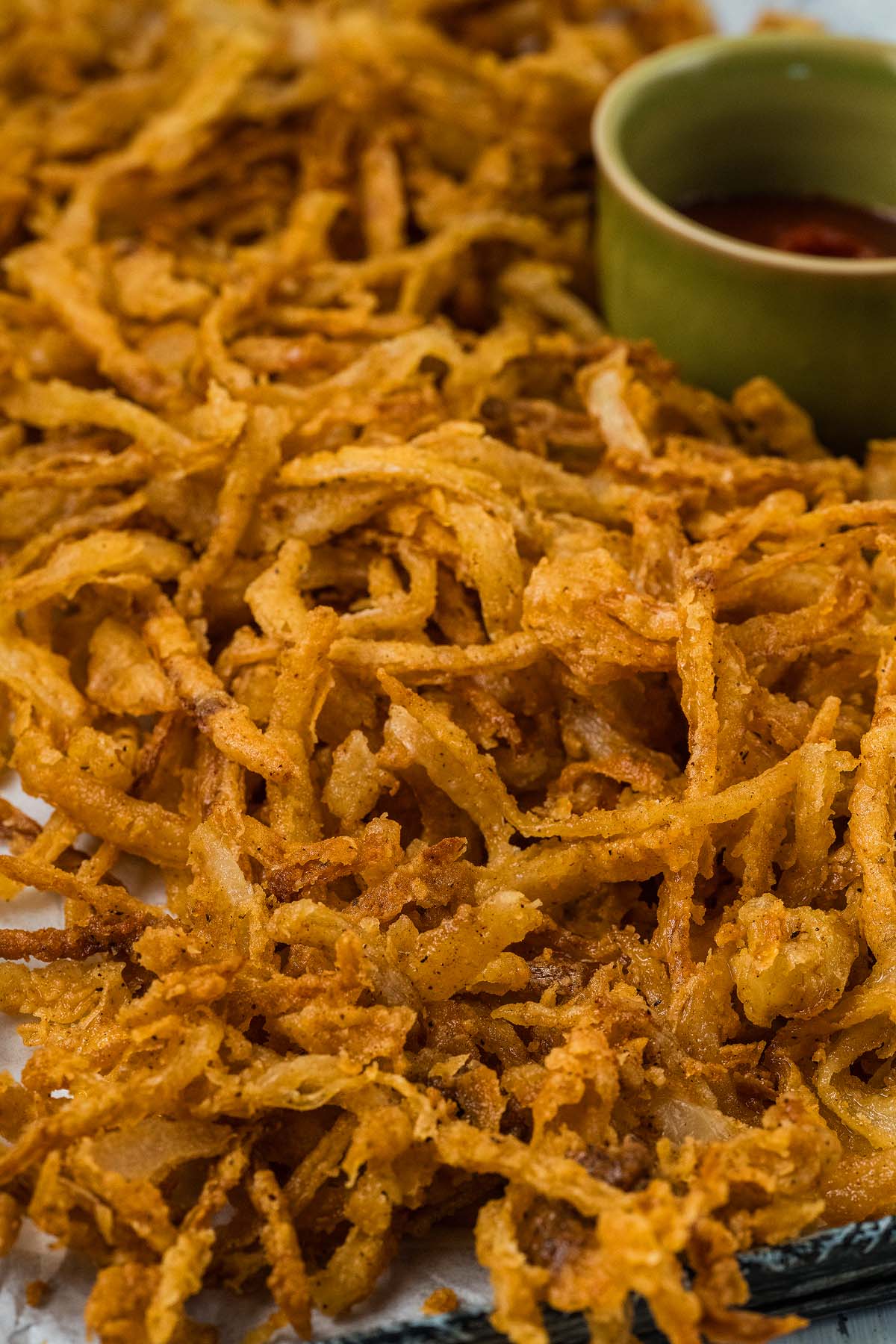 Crispy onion strings are piled high next to a small green bowl of dipping sauce.