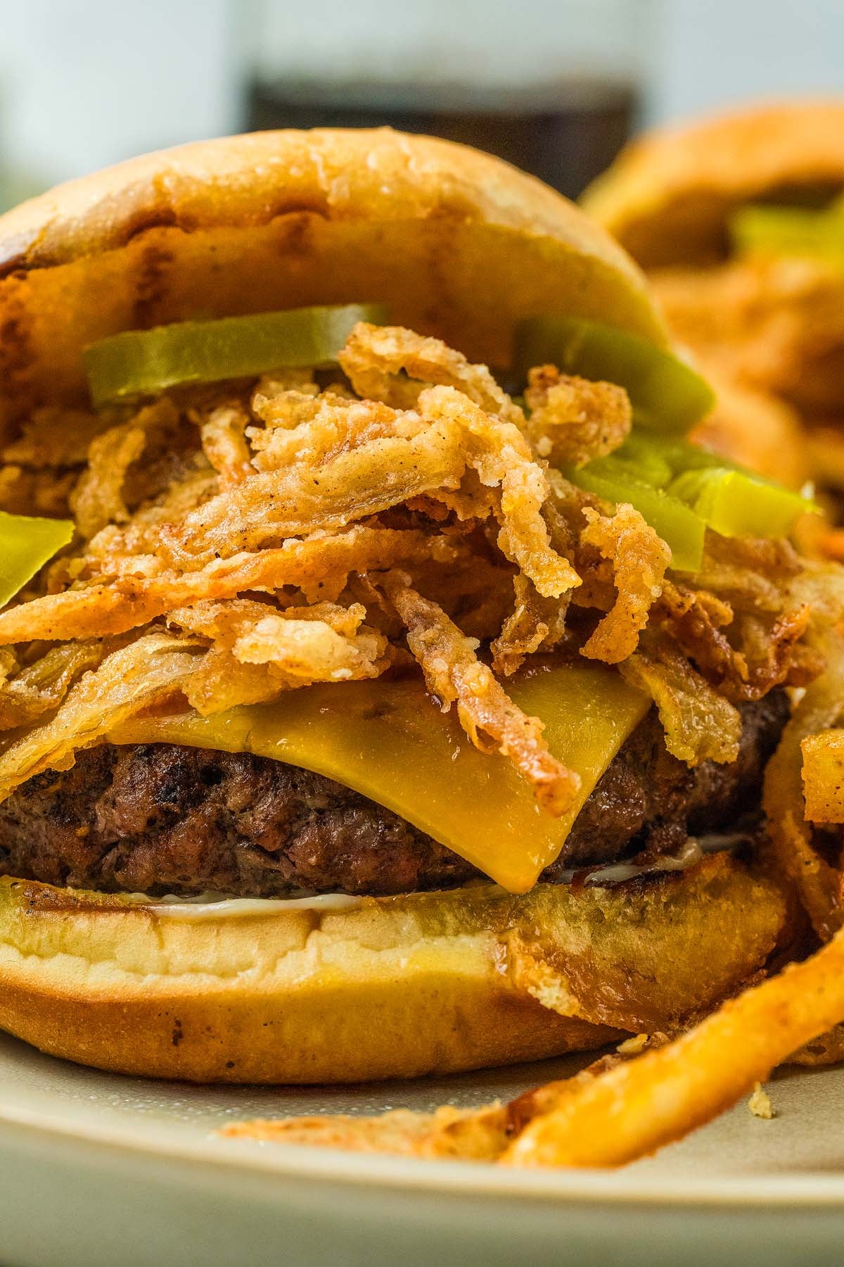 Cheeseburger with crispy onion strings, pickles, and fries on a plate.