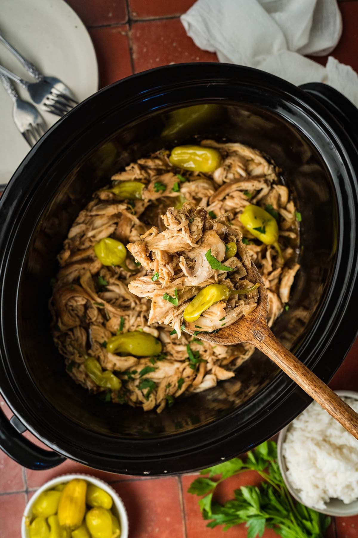 Shredded chicken with peppers in a slow cooker, served with rice and herbs, scooped with a wooden spoon.