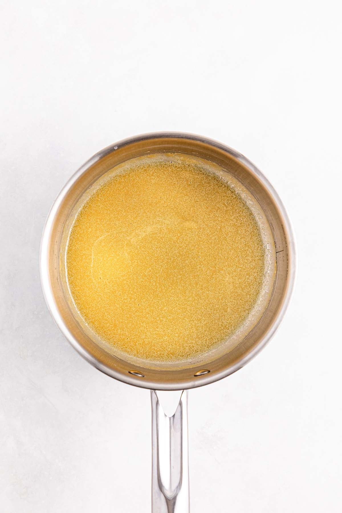 A stainless steel saucepan filled with melted butter, seen from above on a white background.