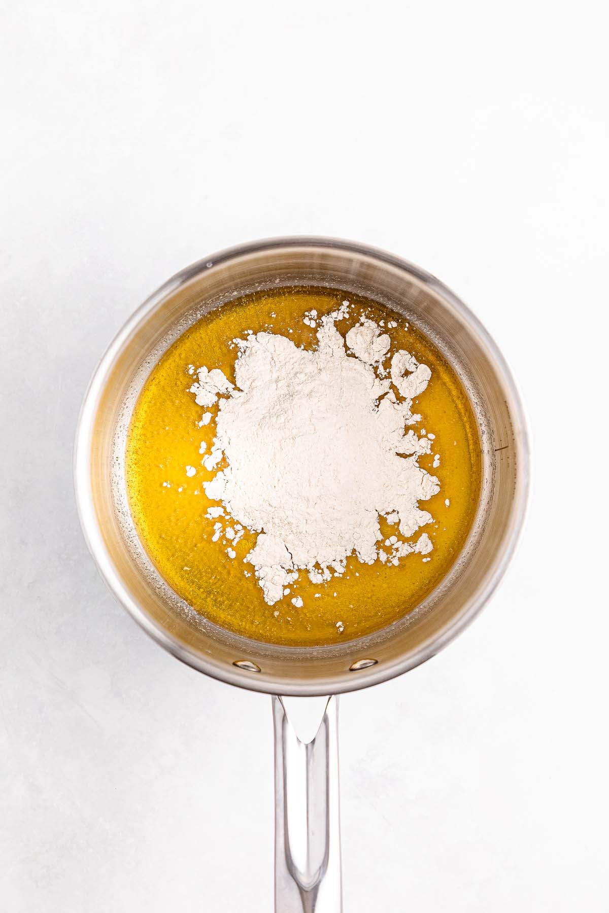 A saucepan with melted butter and a mound of flour on top, viewed from above on a white background.
