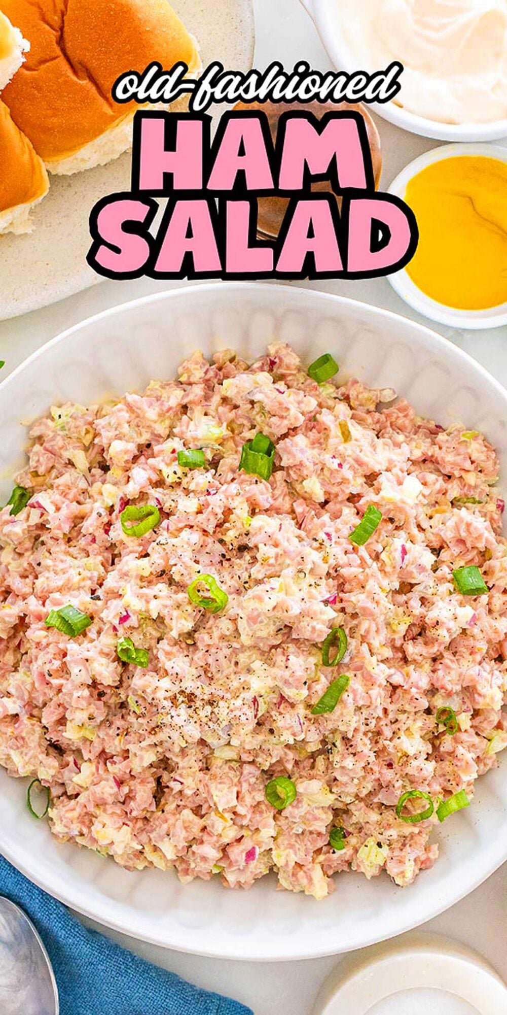 Bowl of ham salad garnished with green onions, surrounded by buns, mustard, and mayonnaise.