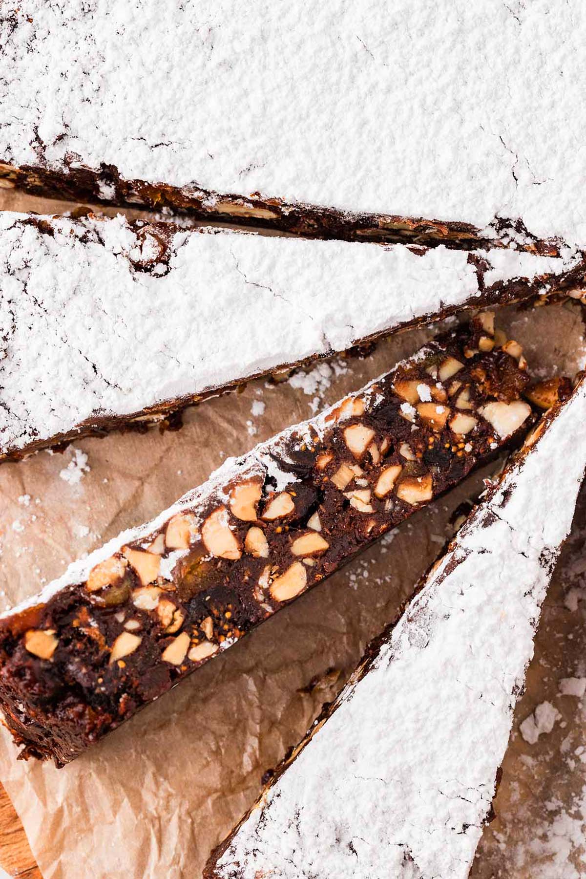 Sliced chocolate nut cake topped with powdered sugar on parchment paper.