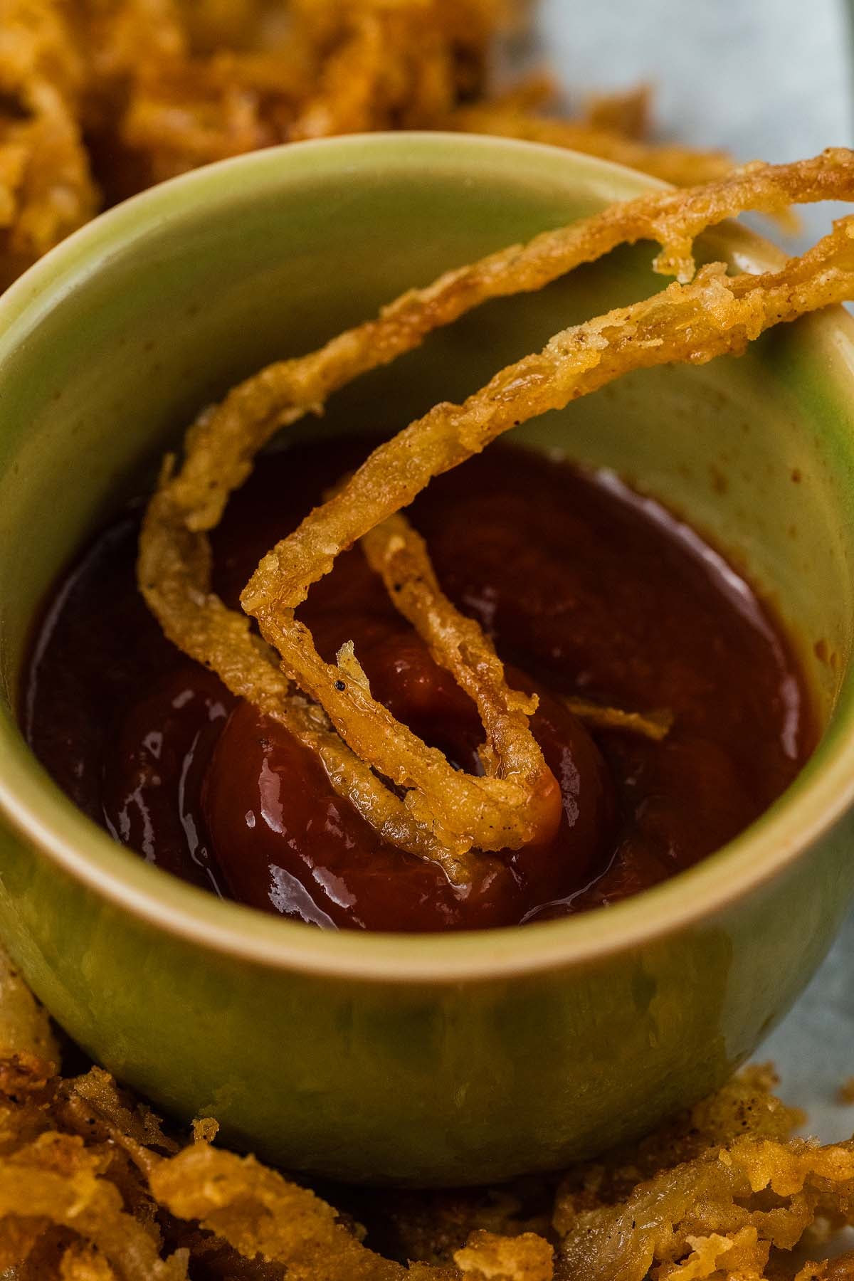 A a handful of crispy onion strings being dipped into a bowl of sauce.