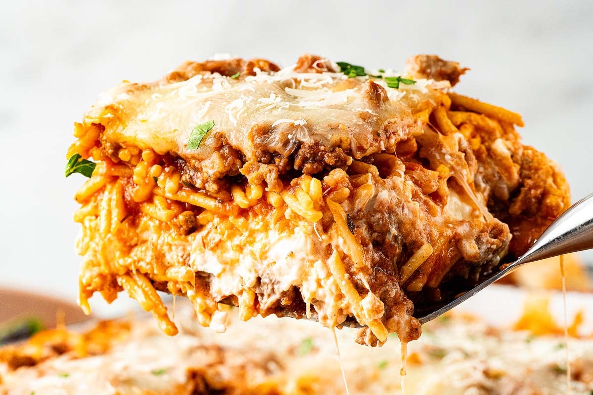 A close-up of a cheesy baked million dollar spaghetti casserole slice topped with ground meat and herbs.