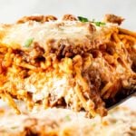 A close-up of a cheesy baked million dollar spaghetti slice with meat sauce being lifted out with a spatula.