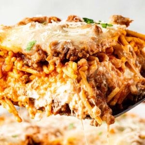 A close-up of a cheesy baked million dollar spaghetti slice with meat sauce being lifted out with a spatula.