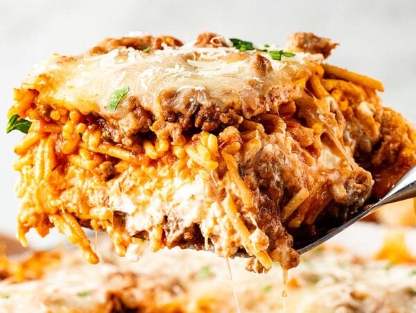 A close-up of a cheesy baked million dollar spaghetti slice with meat sauce being lifted out with a spatula.