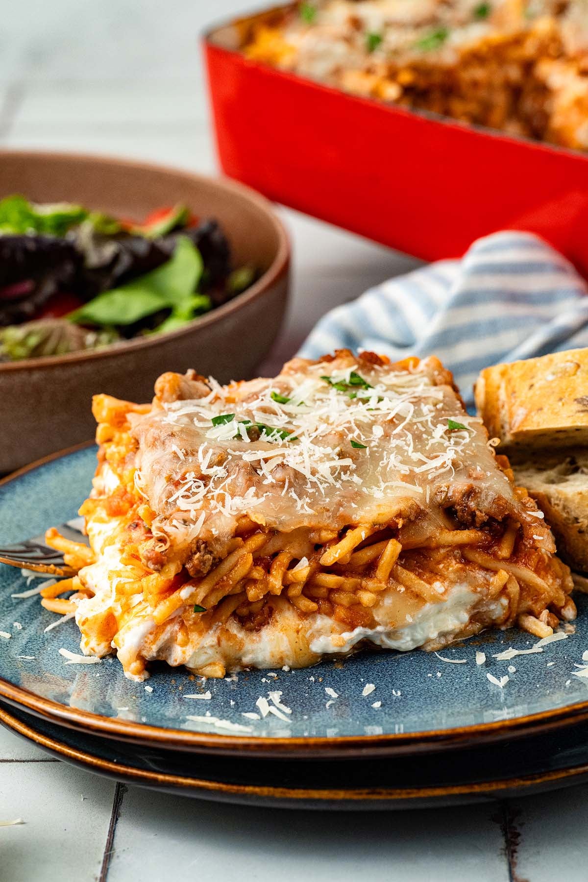 A slice of baked spaghetti with cheese, garlic bread, and salad on a plate.