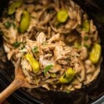 Shredded chicken with peppers and herbs in a slow cooker, served with a wooden spoon.