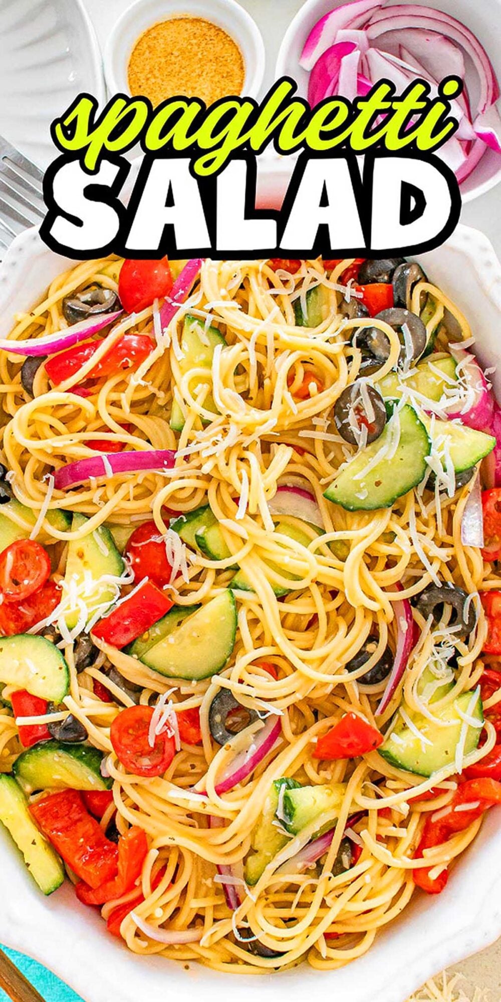 Spaghetti salad with tomatoes, cucumbers, olives, red onions, and shredded cheese in a white dish.