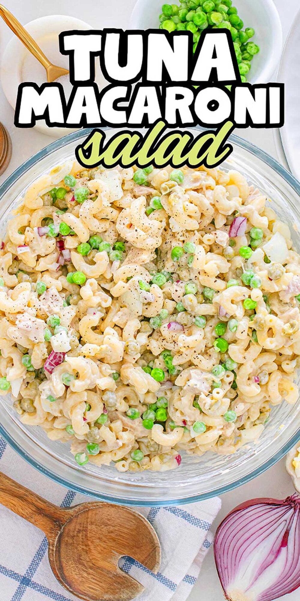 A bowl of tuna macaroni salad with peas and red onion, topped with black pepper, on a white table.