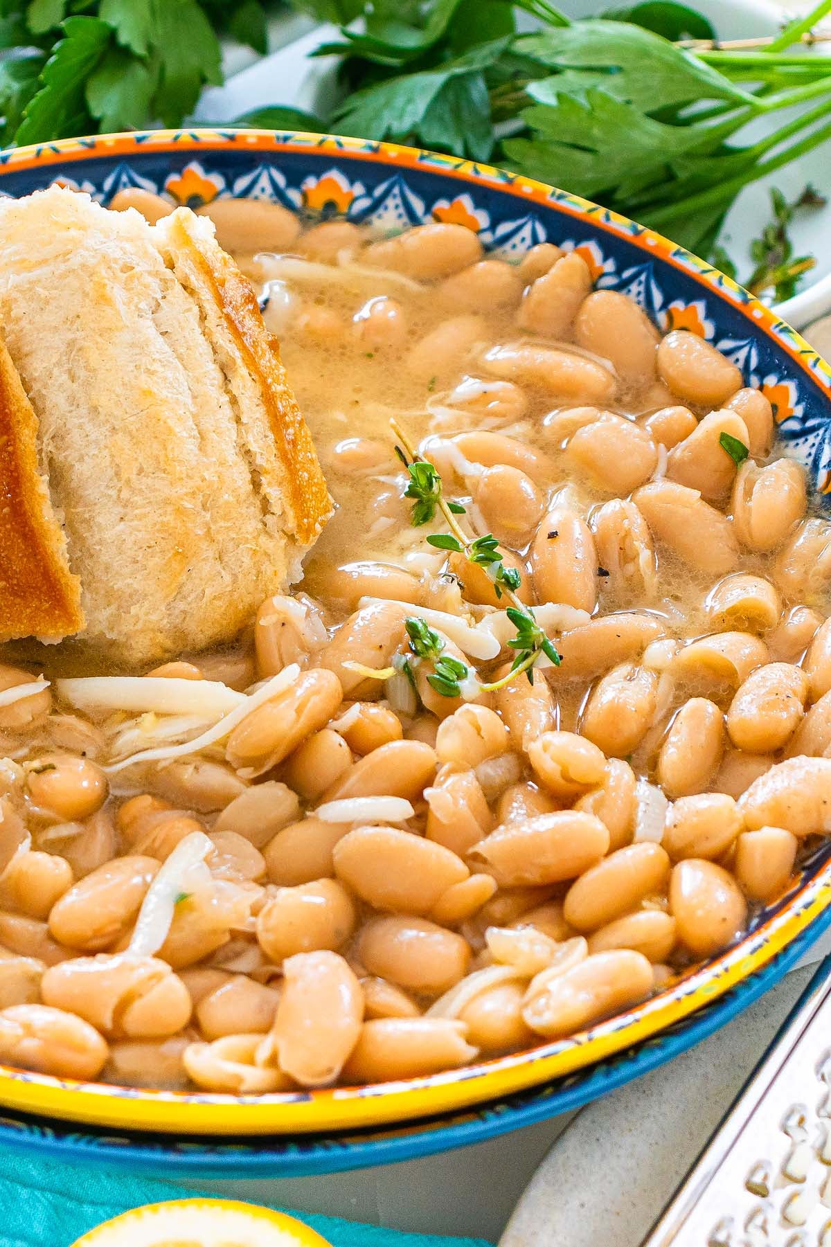 A bowl of Tuscan white beans in broth with herbs, topped with bread, garnished with parsley in the background.