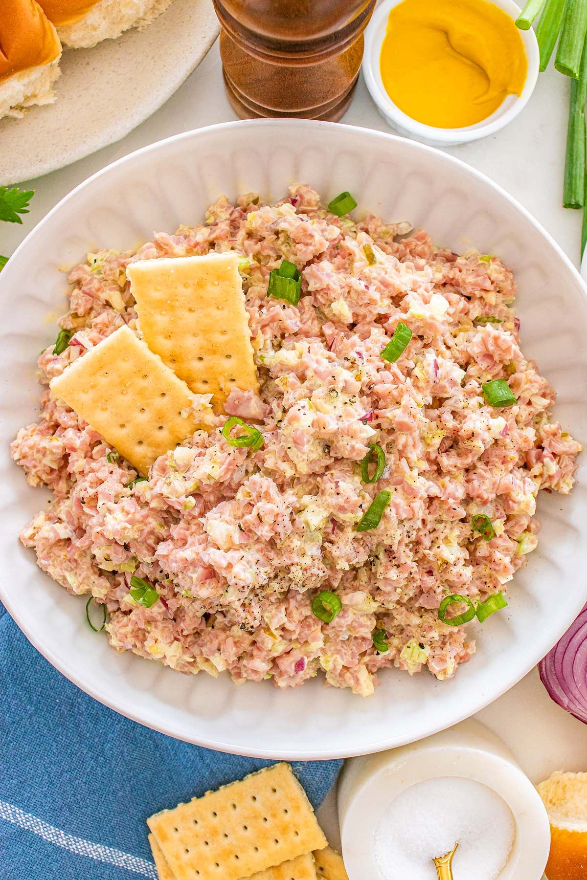 A bowl of creamy ham salad topped with sliced green onions and served with crisp saltine crackers.