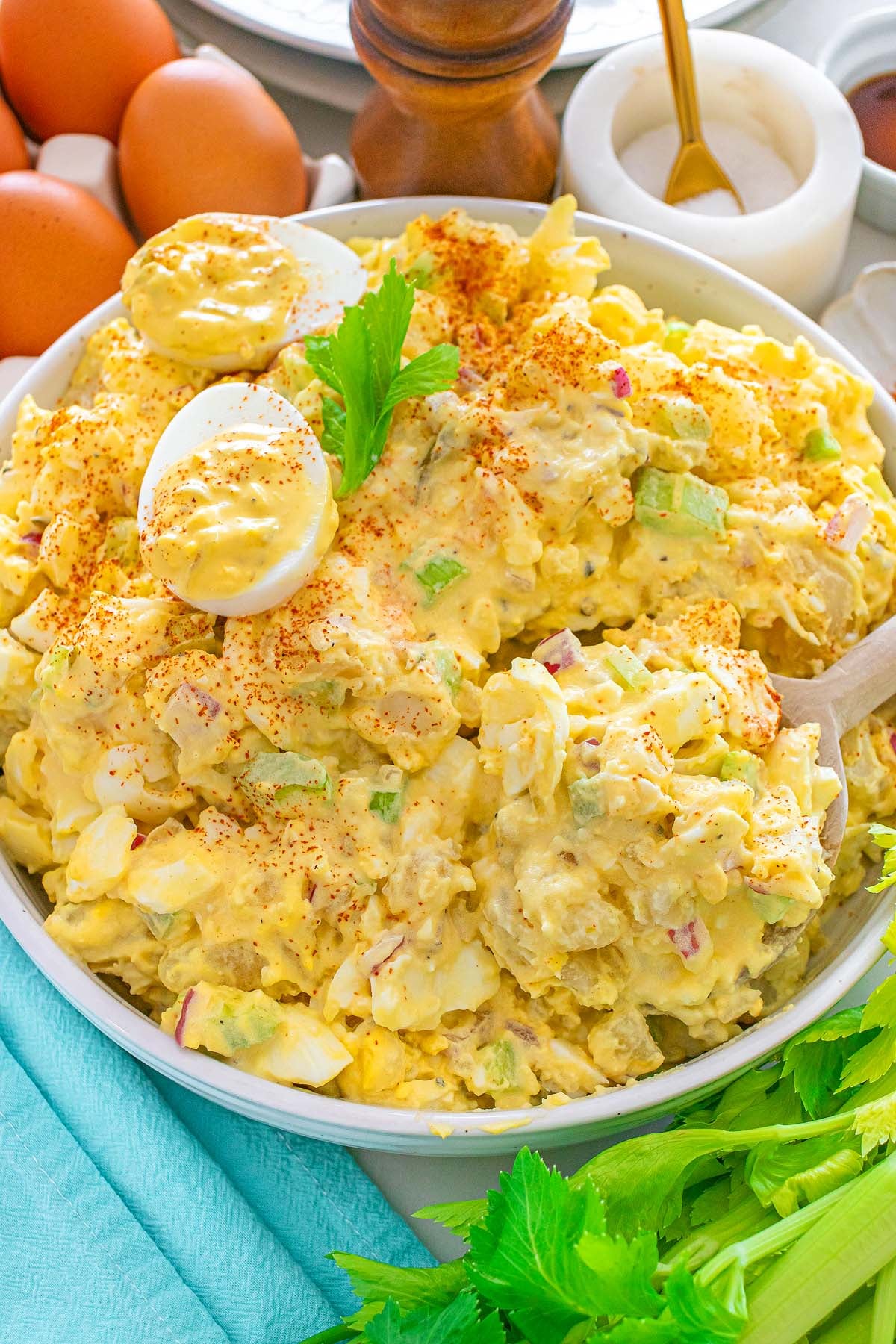 Bowl of creamy potato salad with boiled eggs, celery, and paprika, garnished with parsley.