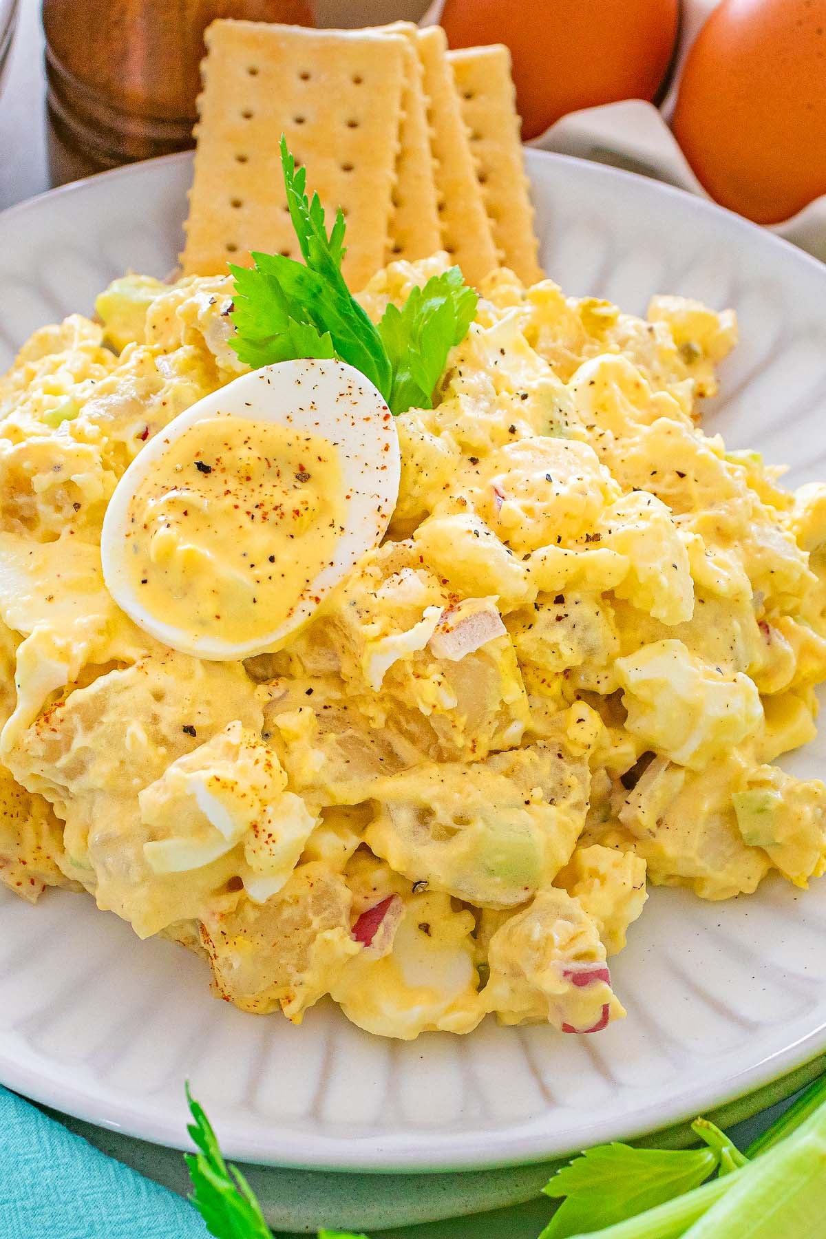 Egg salad with sliced boiled egg on top, garnished with celery, served with crackers on a white plate.