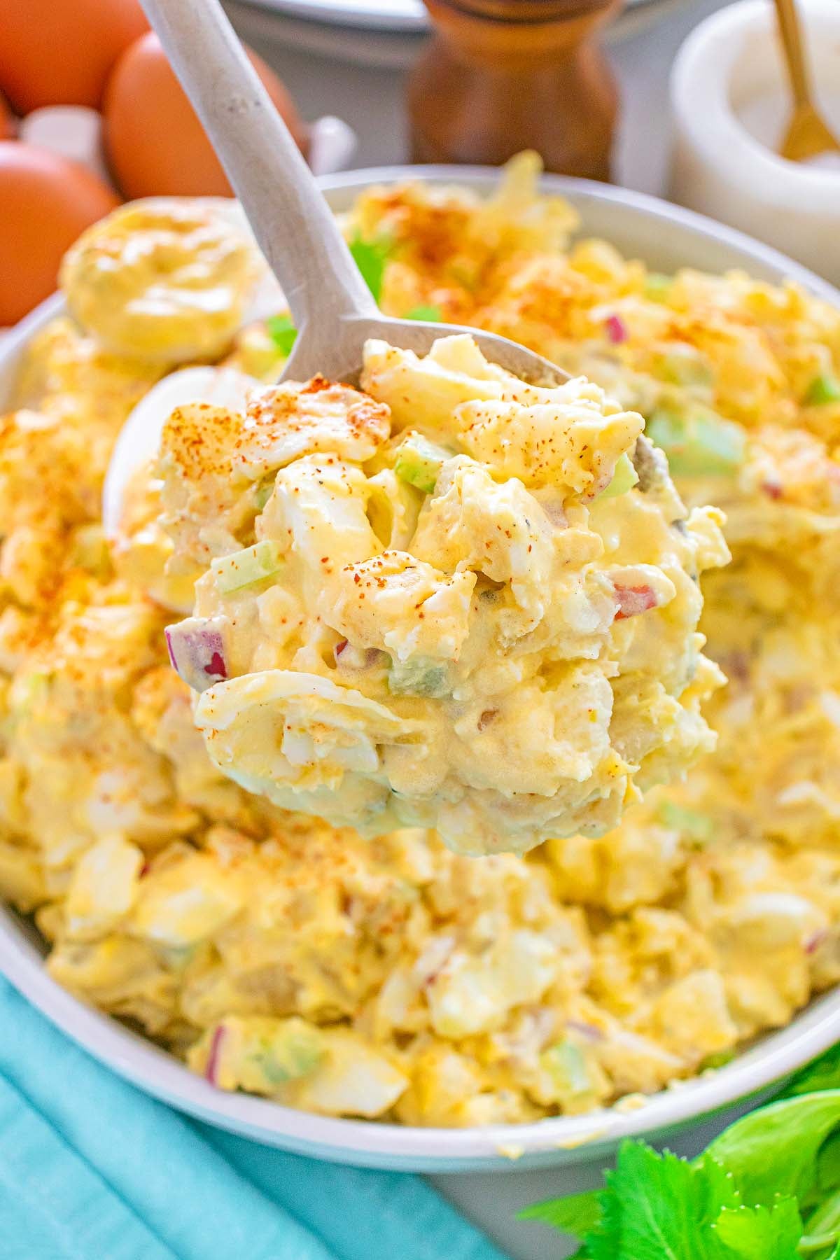 A spoonful of creamy potato salad with chopped eggs, celery, and red onions, sprinkled with paprika.