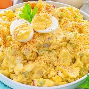 Bowl of potato salad topped with sliced boiled eggs and paprika, with eggs and celery nearby.