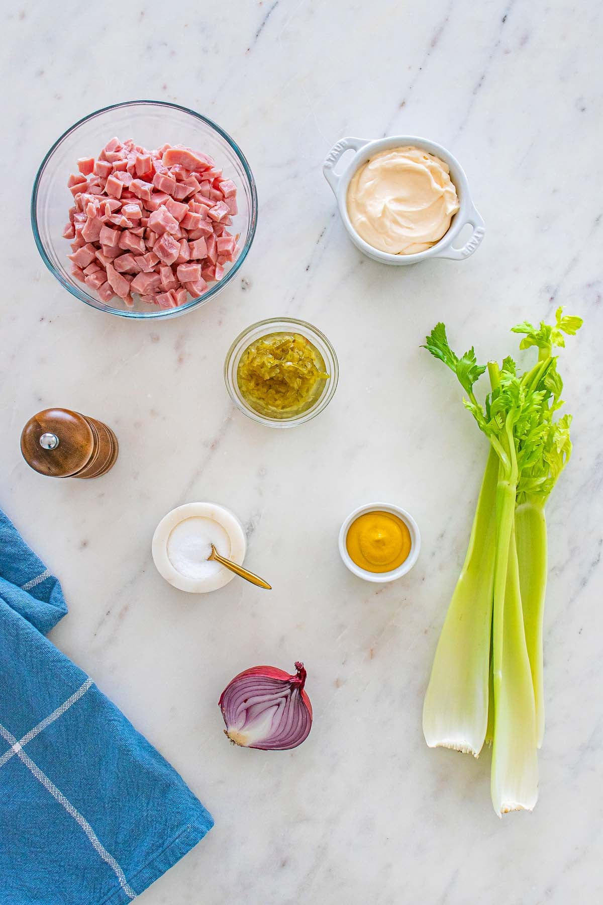 Ham salad made with chopped ham, mayonnaise, relish, mustard, celery stalks, red onion, salt, and pepper on a marble counter.