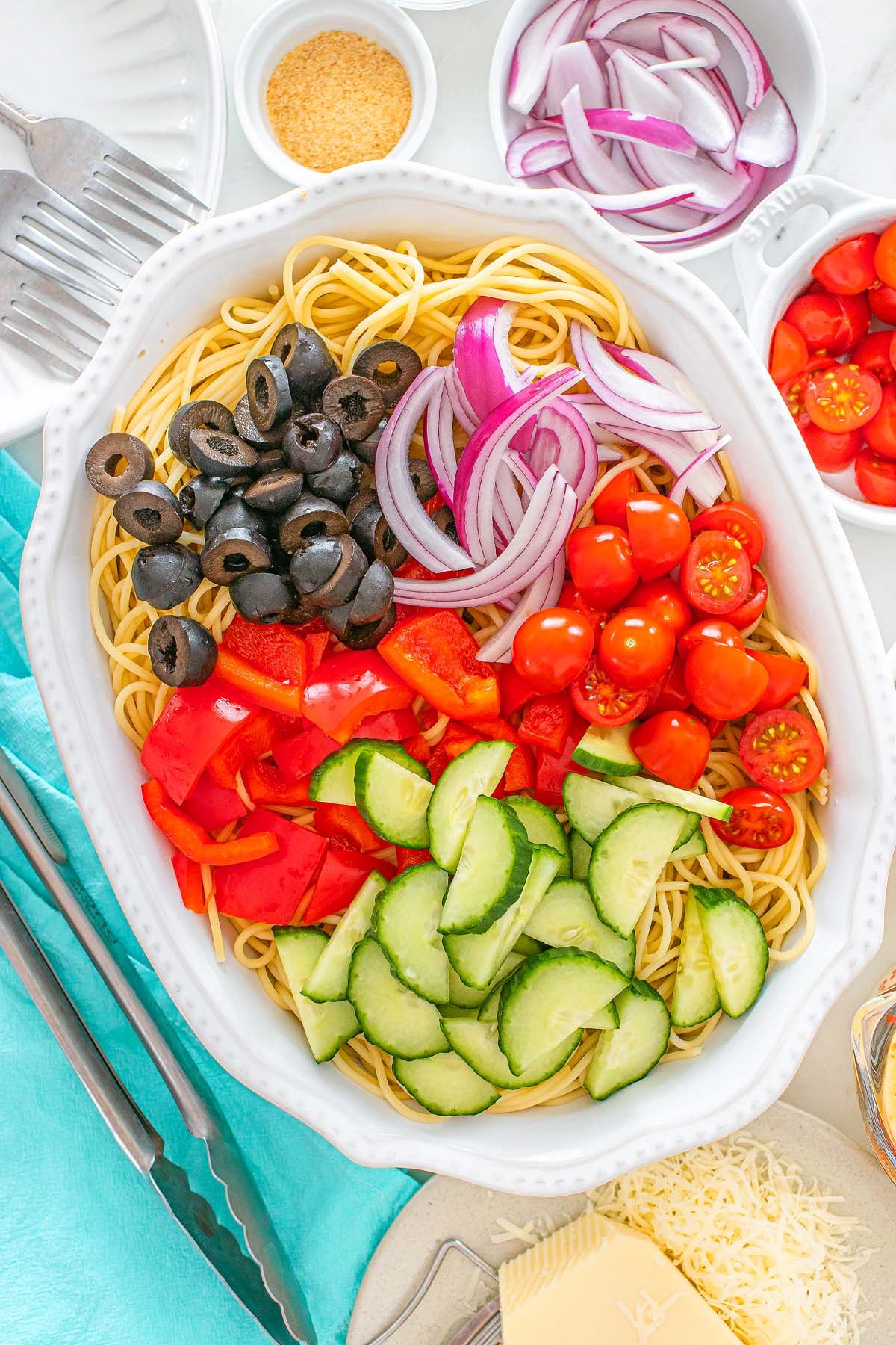 Spaghetti topped with sliced black olives, red onions, cherry tomatoes, red peppers, and cucumbers.