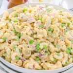 A bowl of creamy tuna macaroni salad with peas, diced red onions, and black pepper on top.
