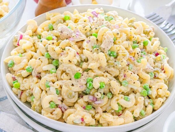 A bowl of creamy tuna macaroni salad with peas, diced red onions, and black pepper on top.