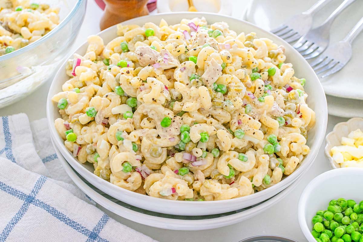 Bowl of tuna macaroni salad with peas, diced red onions, and a creamy dressing on a white table.