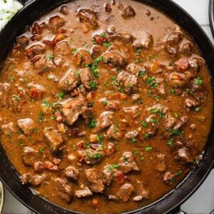 Beef tips and gravey in a black skillet, served with mashed potatoes, green beans, and plates with forks on the side.