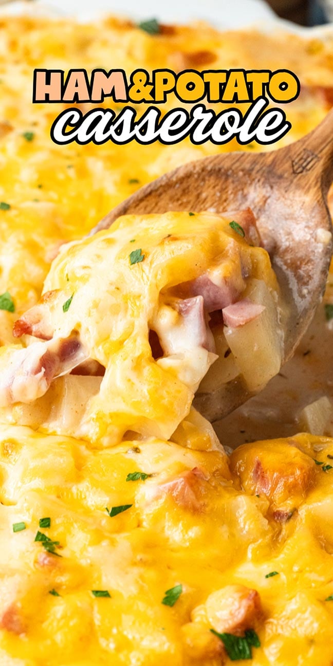 A wooden spoon scoops cheesy ham and potato casserole with melted cheese and herbs on top.