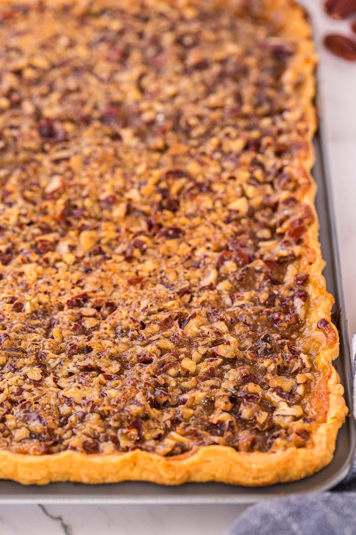 Close-up of a rectangular pecan pie slab with a golden crust and nutty topping on a baking sheet.