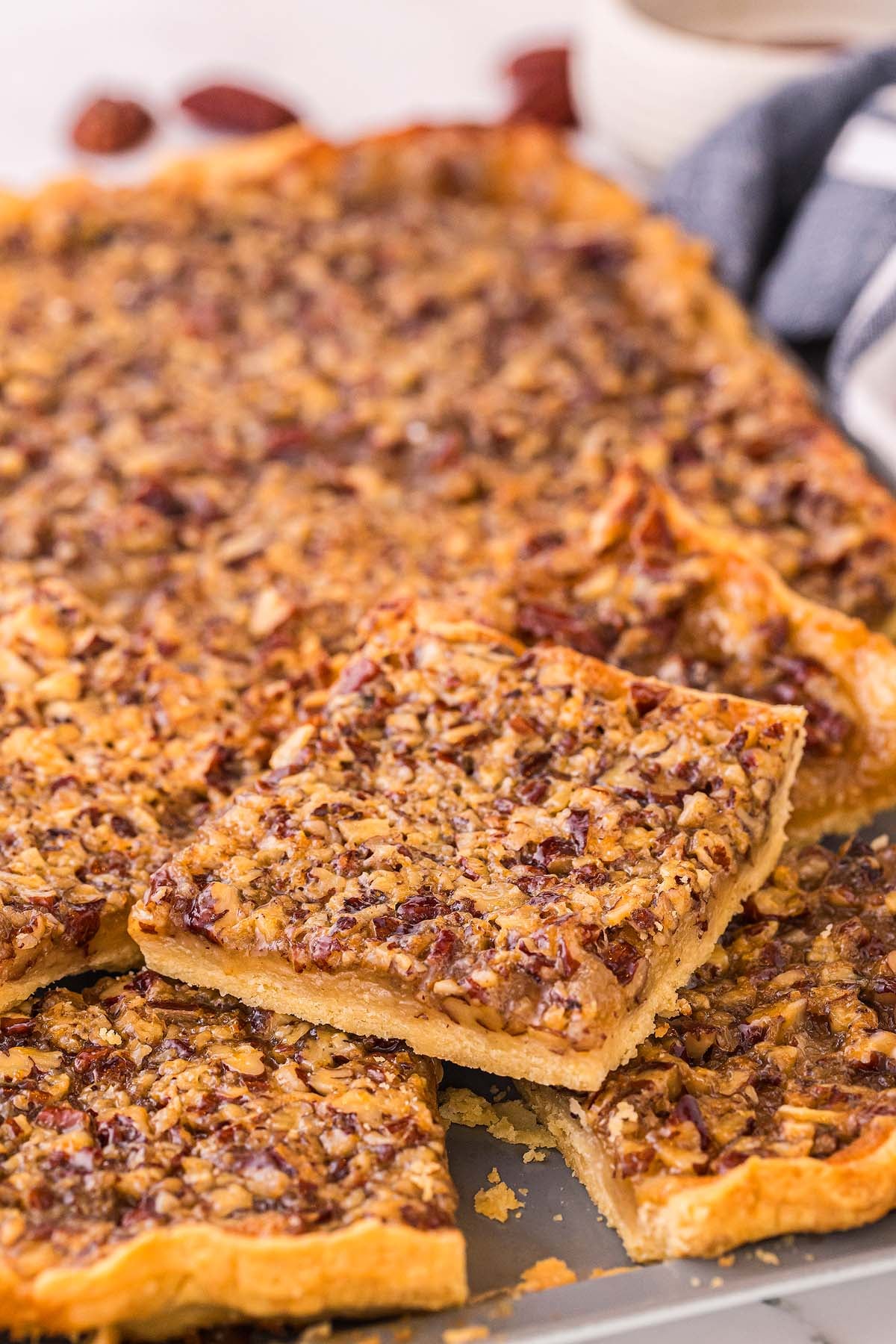 Close-up of pecan slab pie squares, with a golden crust and nut topping, stacked on a tray.
