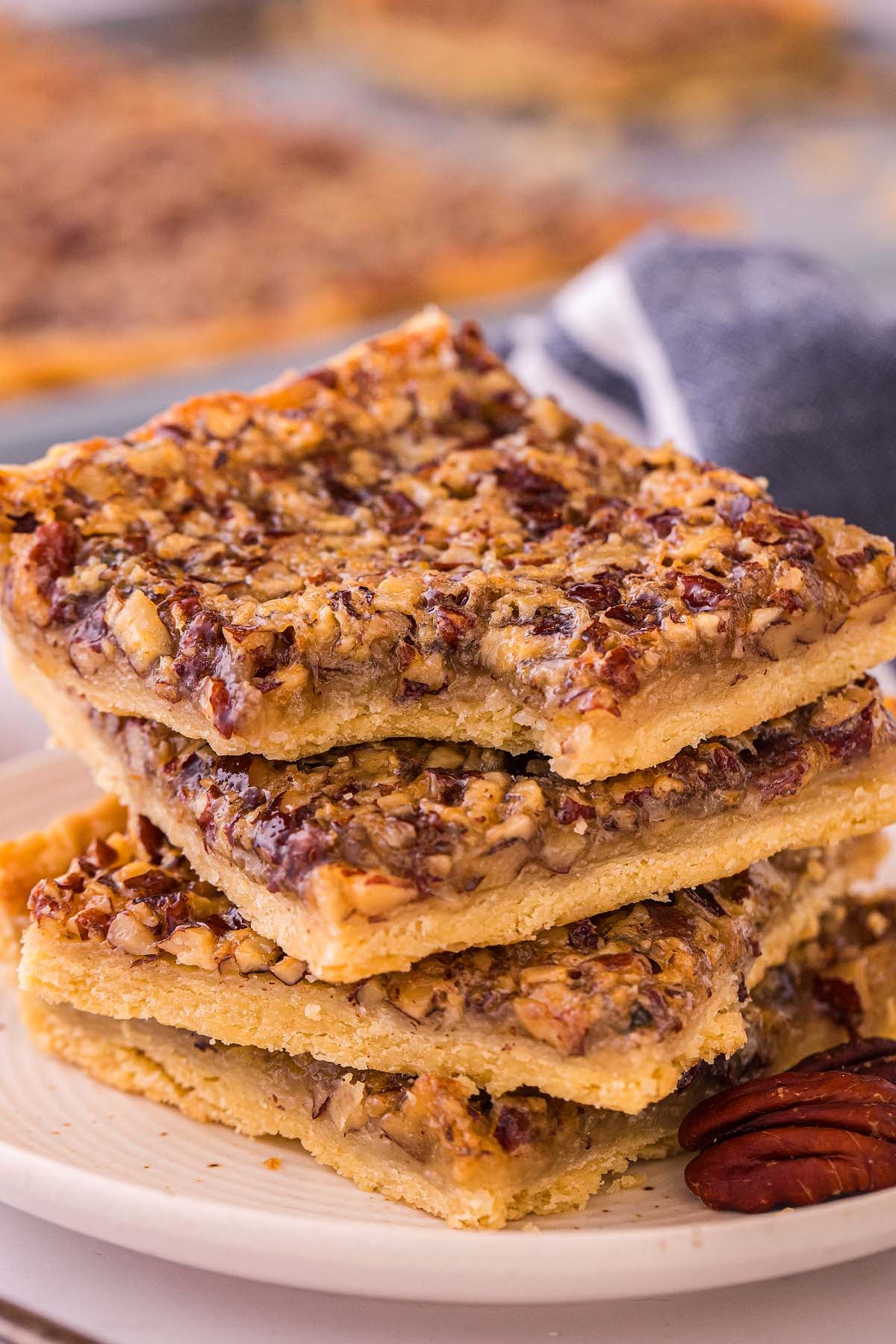 Three pecan pie squares stacked on a white plate, showing their nutty filling and golden crust.