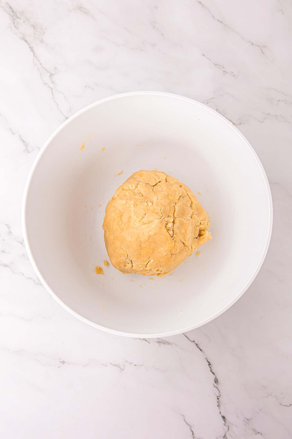 A ball of dough sits in a large white bowl on a marble countertop.